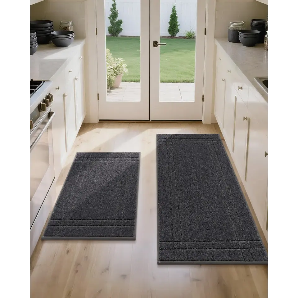 Two gray kitchen rugs on a wooden floor with a view of a garden through French doors.