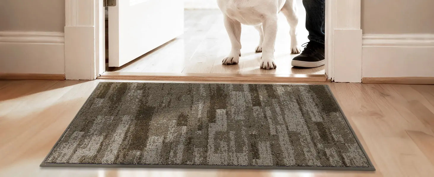 Gray doormat on a wooden floor with a dog entering through a glass door.